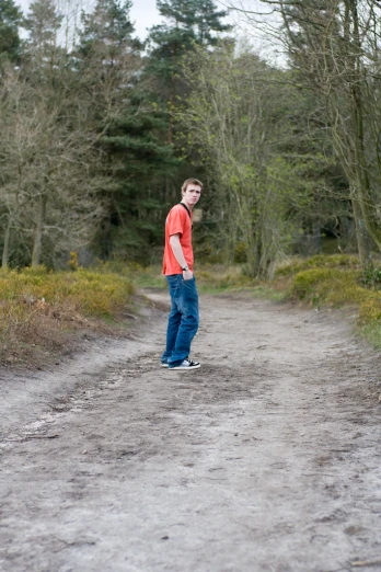 a man in an orange shirt stands on a road in the woods