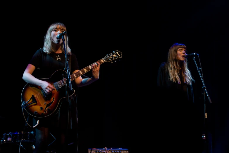 two young women playing guitars while they sing at the same time