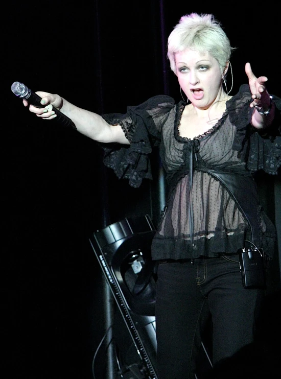 a woman with white hair and a black shirt is standing on a stage holding her hand up