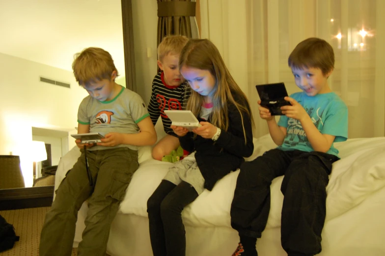 three children playing on tablet devices on a bed