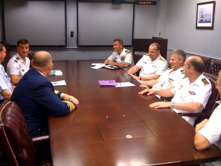 a group of men sit at a long conference table