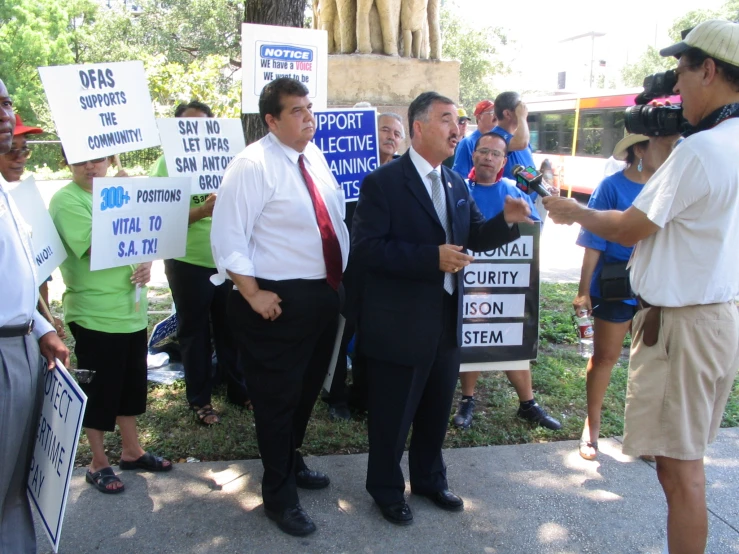 man in suit and tie speaking to protesters holding up signs