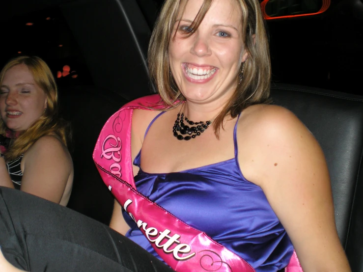 a woman with a pink sash sitting in the back seat