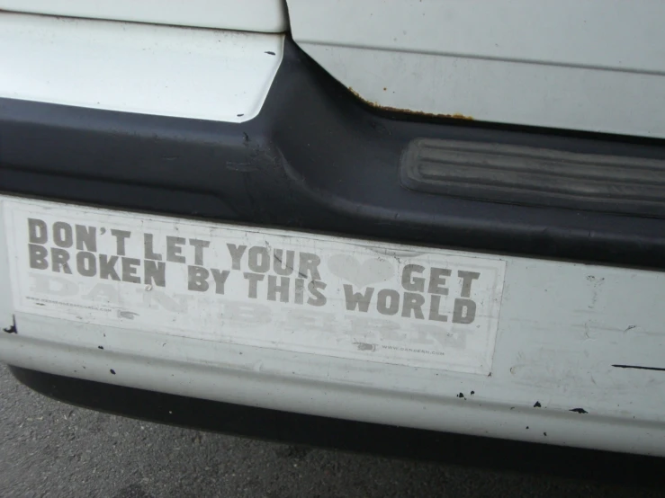a broken down white car has a sign saying don't let your get broken by this world