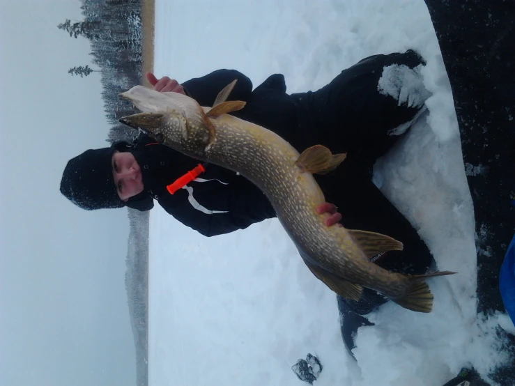 a man sitting in the snow holding a large fish