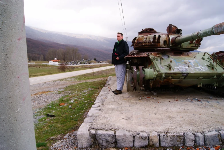 man standing next to destroyed tank in outdoor setting