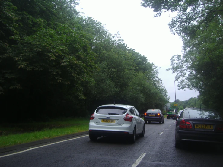 three cars are driving down the road by trees