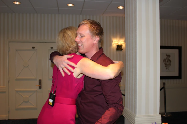 a woman in a red dress hugging a man who is dressed in maroon