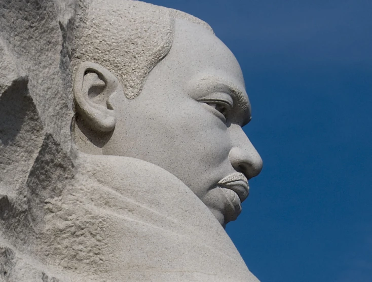 a large statue with a bald face is in front of a blue sky