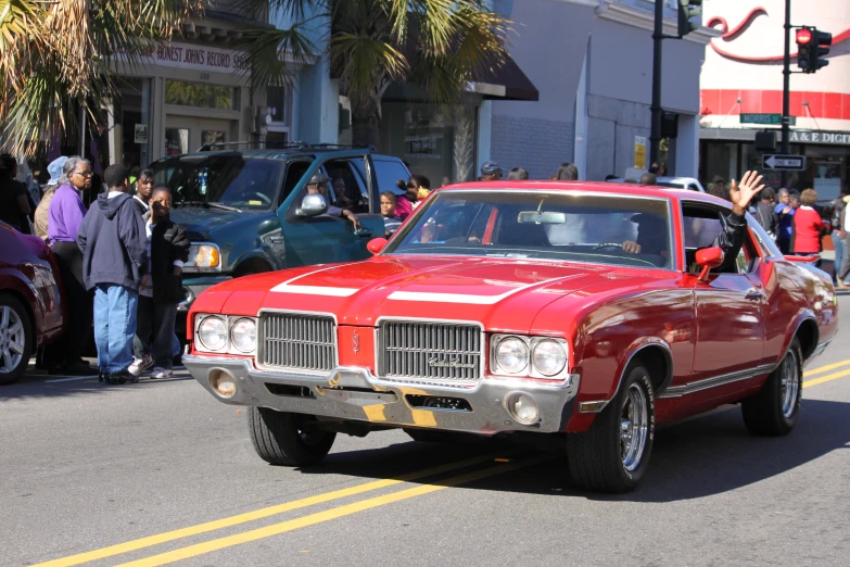 a large red car driving past people on the side of the road