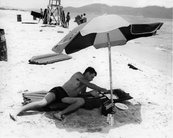 a man sitting in the sand with an umbrella