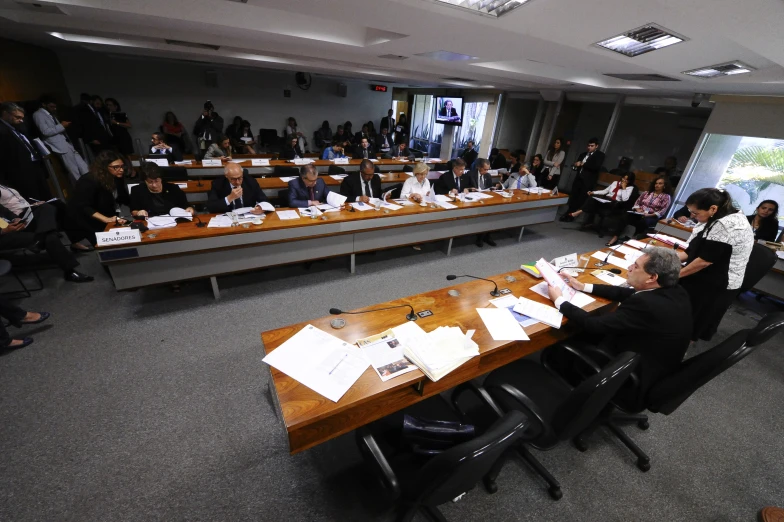 a room with people sitting around tables, in rows of chairs