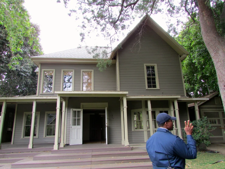 a man standing outside of a gray house with a lot of trees