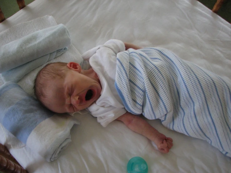 an infant in blue pajamas is yawning with his mouth open