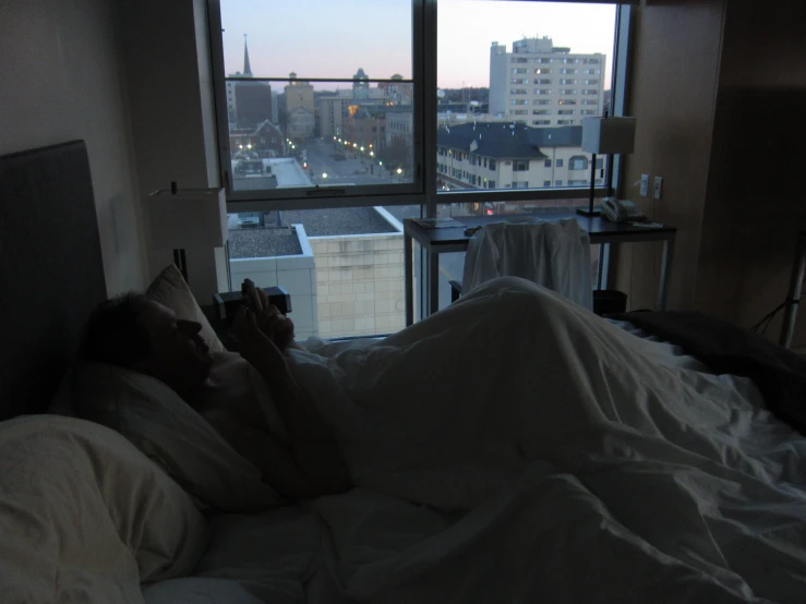 a person in bed watching the sunset with city seen through window
