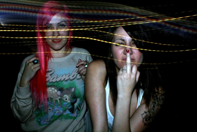 two girls with bright, brightly colored hair pose in front of a string of lights