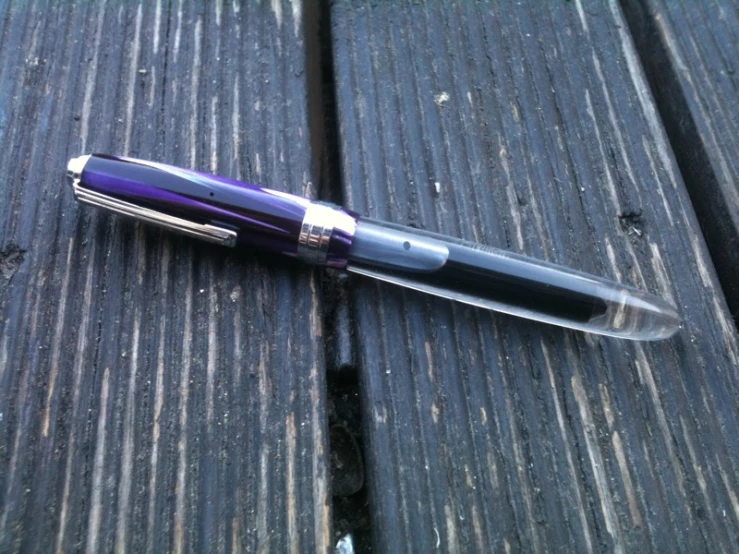 a pen with a purple cover laying on a wooden surface