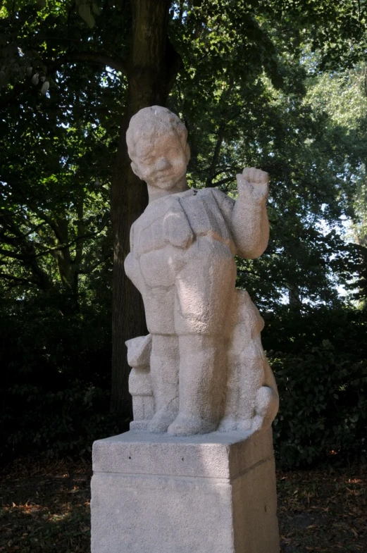 a stone statue of a boy sitting in the park