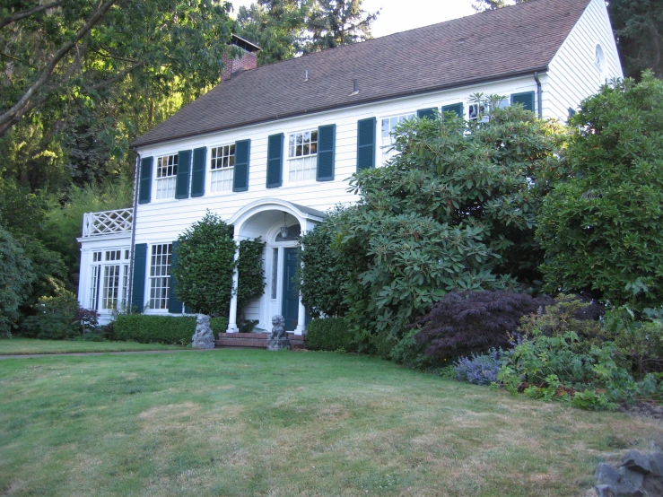 a large white house with green shutters and a porch on the second story