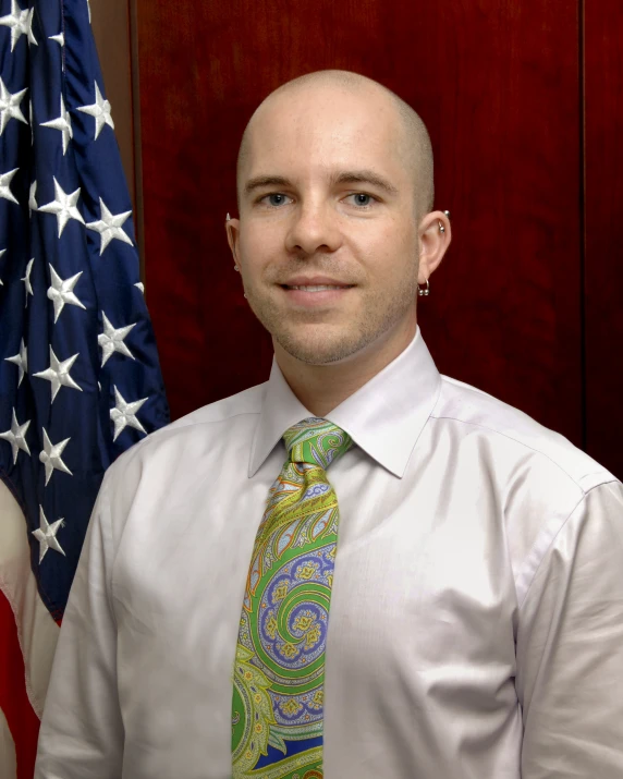 a bald man standing in front of two flags