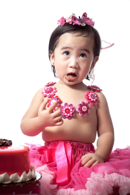 a young baby sitting in front of a cake wearing a pink dress