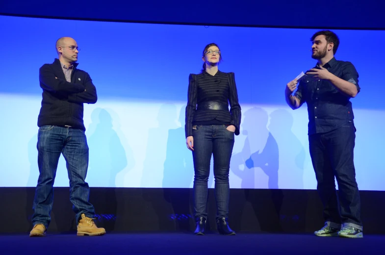 four people standing on stage one of them is wearing jeans