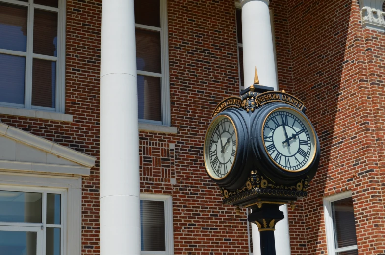 a black clock with two white faces on a pole in front of a brick building