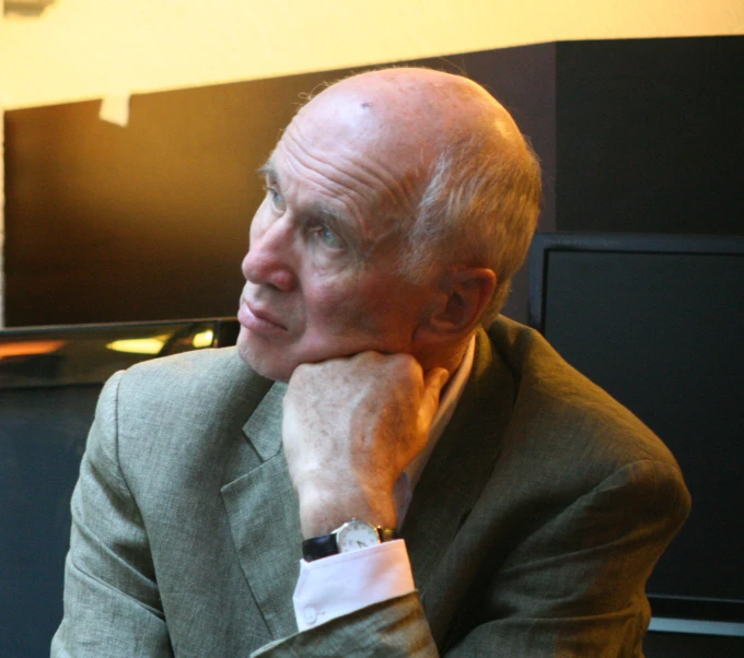 an older man wearing a suit and tie looks over his shoulder