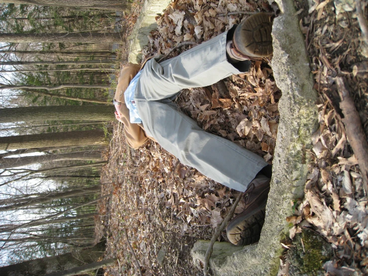 man laying on leaf covered ground with a teddy bear in the woods