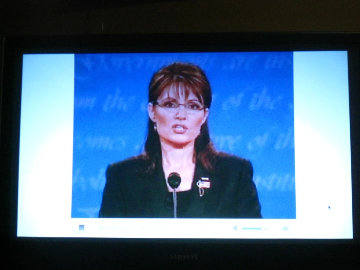 a woman in glasses standing at a podium talking to someone