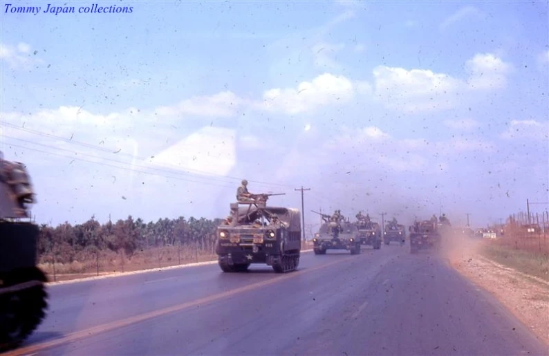 some military trucks drive down the street with a flag