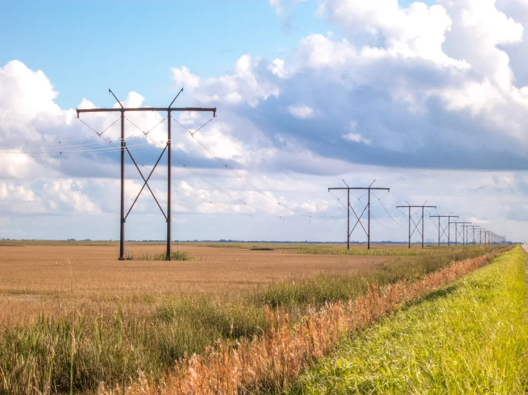 four telephone poles over an empty field with clouds in the background