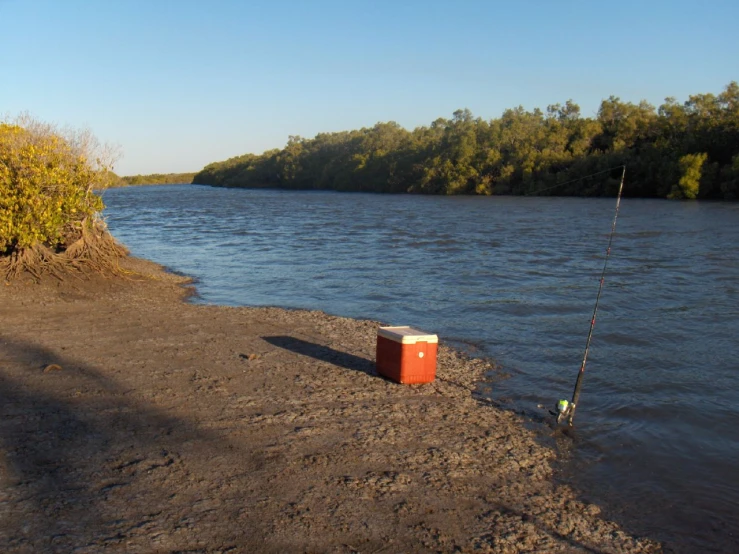 a red box is standing in the water by some shore