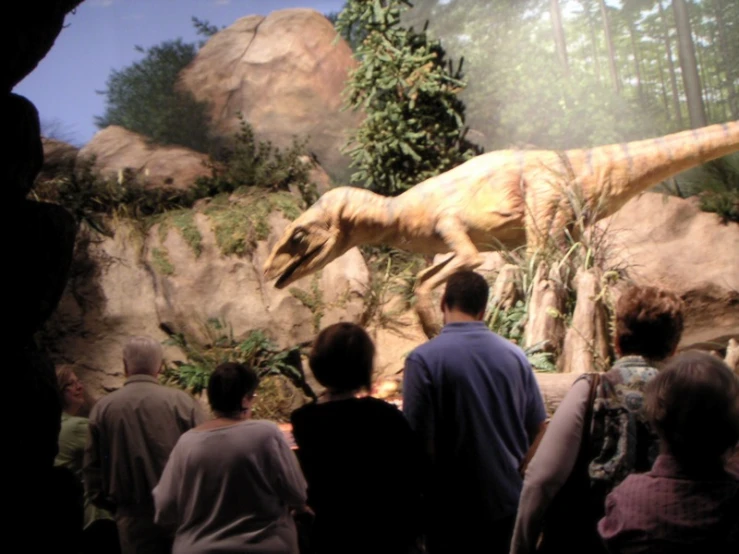 some people looking at a fake t - shirt dinosaur in a museum