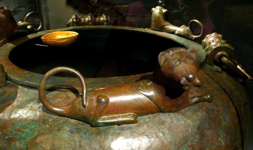 an ancient metal urn with a gold bowl and handles