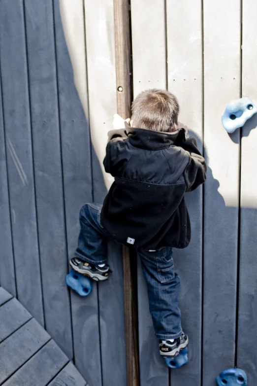 a little boy standing on top of a wooden fence