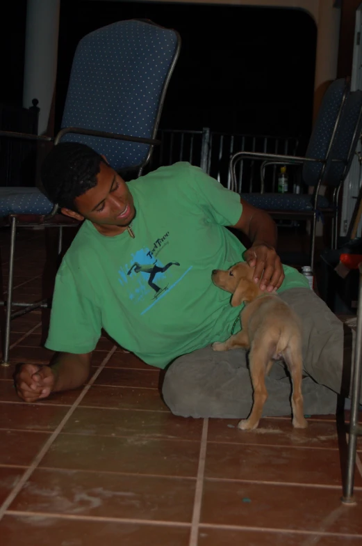 a man in a green t shirt sitting on the floor with his dog