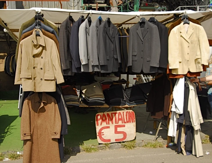 several suits and ties hanging on racks and other clothing at a clothing stand