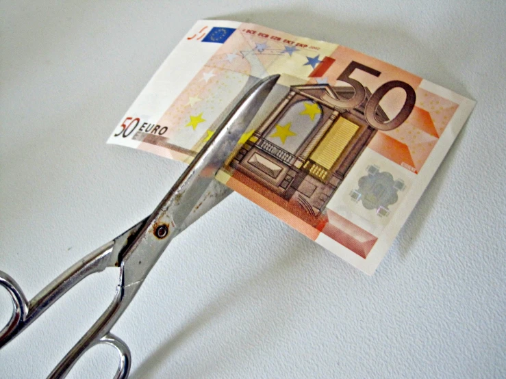 a pair of scissors holding fifty euros bills