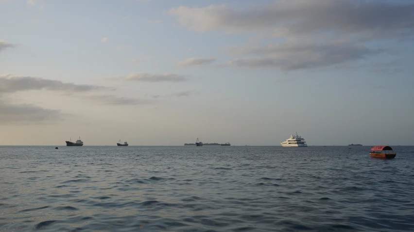 several boats sailing in the ocean, under cloudy skies