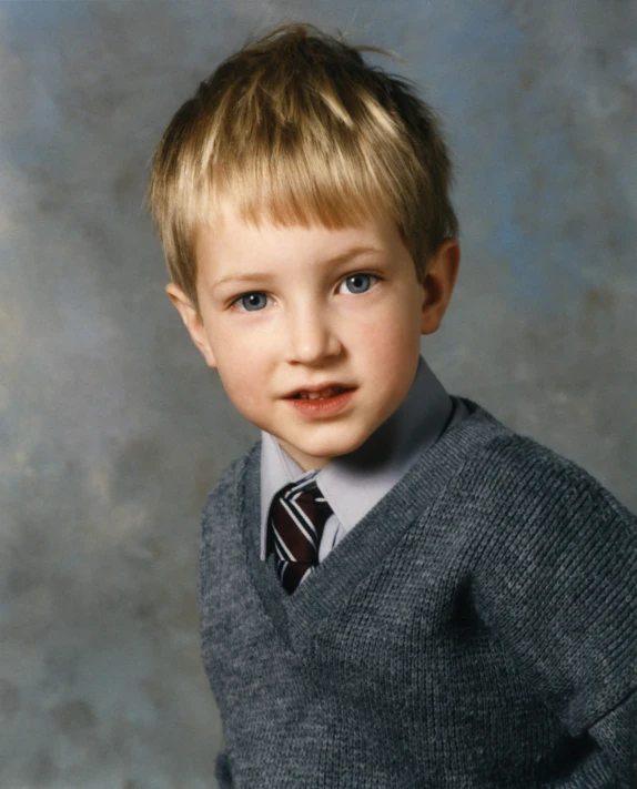 a little boy with blond hair wearing a sweater and tie