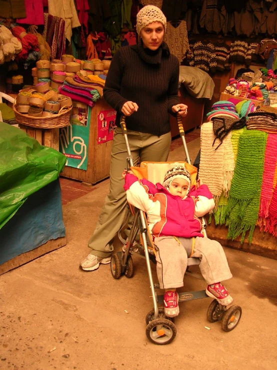 a child in a stroller and a young woman with a hand bag at an outdoor market