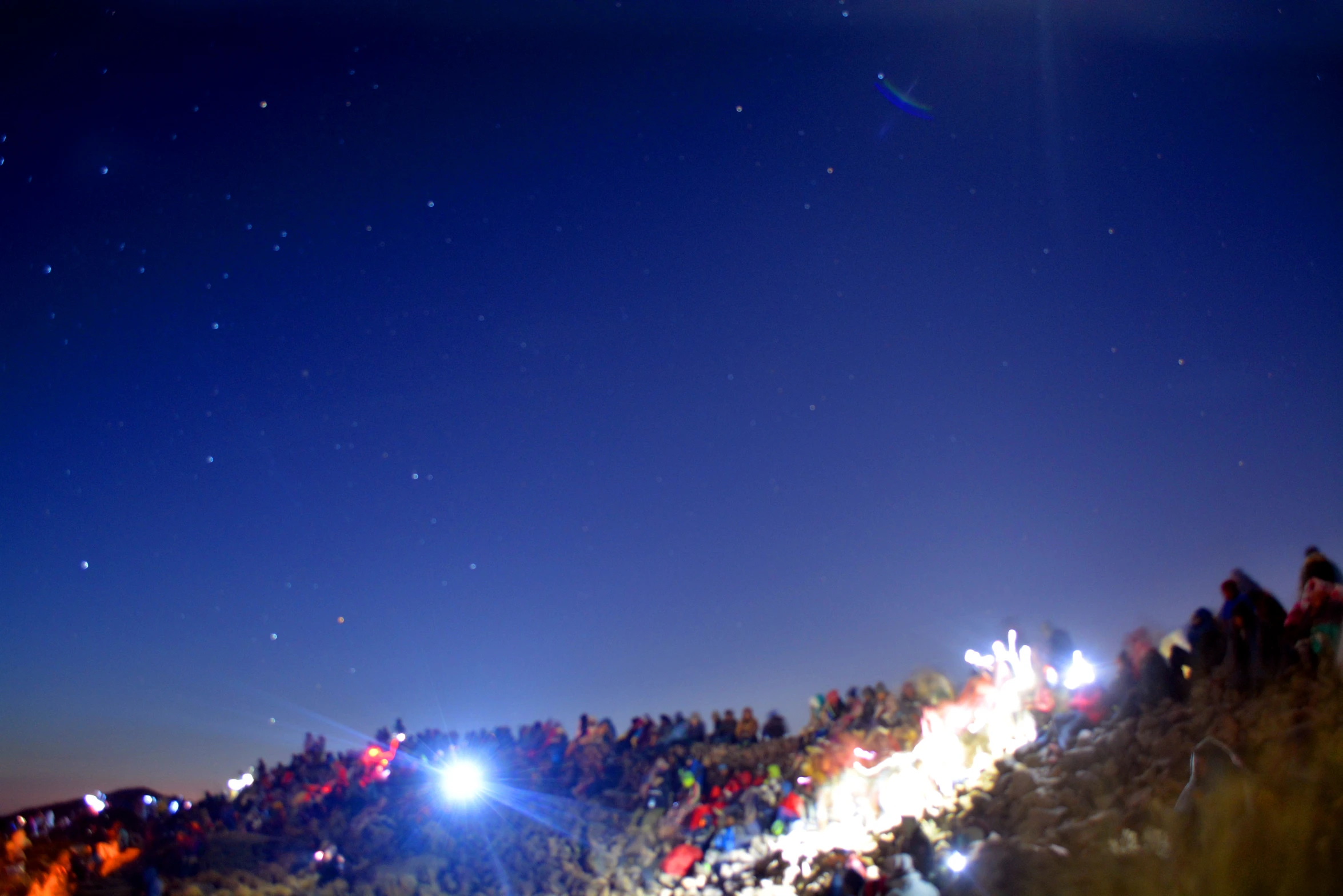 a bunch of people at night time with a hill in the background