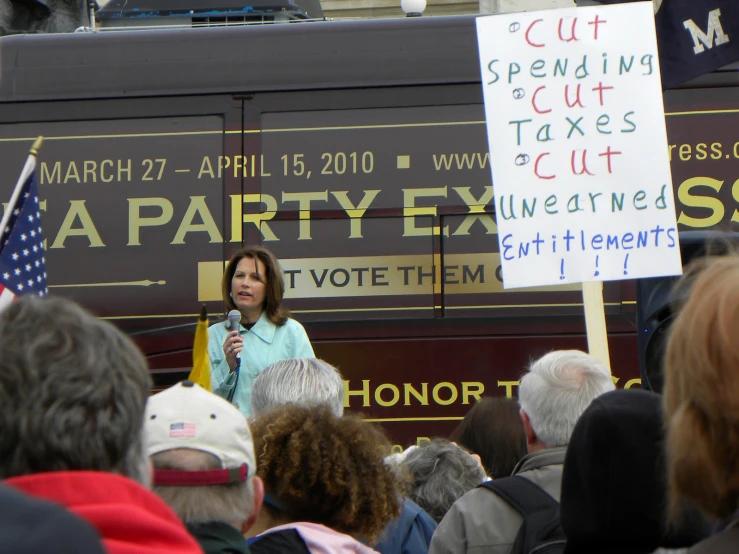 woman speaking at a rally, next to a political bus
