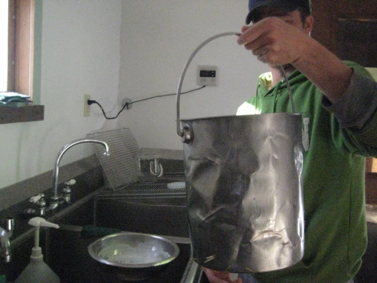 a man in green shirt holding up metal pot