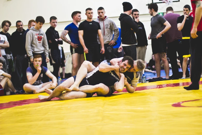 two wrestlers fighting on the ground with an open crowd watching
