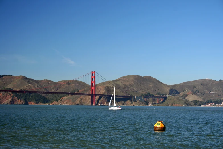 two sailboats sailing in the water near a bridge