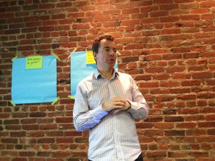 a man in front of a brick wall holding a paper with notes on it