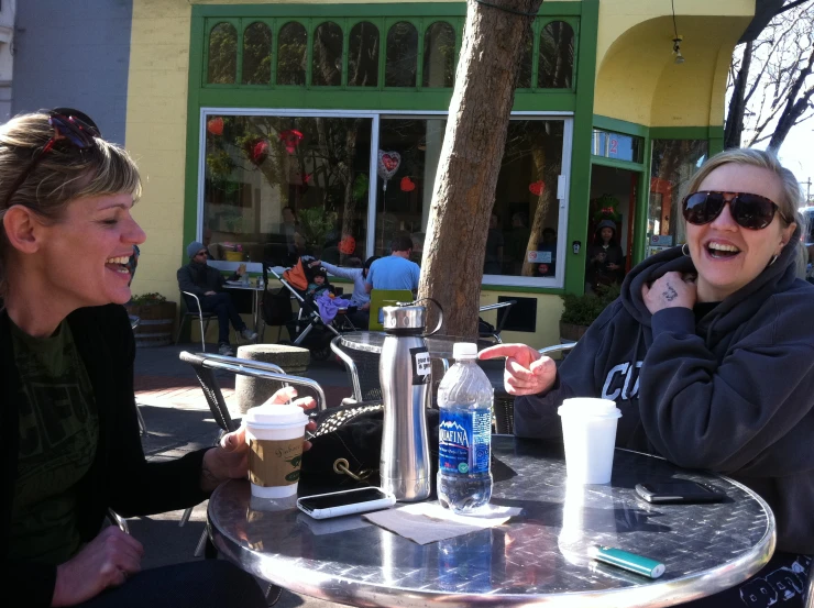 two women are sitting at an outdoor cafe table