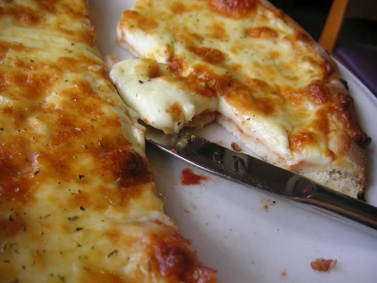 cheese pizza on a white plate with a pizza cutter